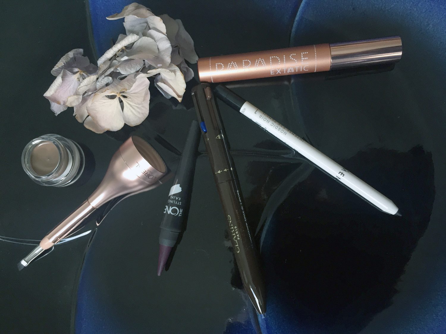 Vasemma L'Oréal Paris Paradise Pomade Extatic -kulmaväri sävy 103 Chatain, Oriflame The One Styling Kajal -rajausväri sävy Purple Intensity, Clarins Stylo 4 Color All-in-One Eyes & Lips -kynä, Lumene Nordic Noir Intense Eye Pencil -rajausväri ja L'Oréal Paris Paradise Extatic -ripsiväri.
